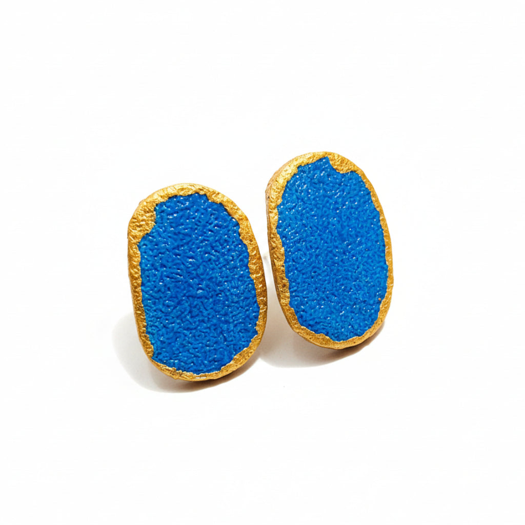 Blue earrings with gold accents on a black and white patterned background