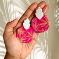 Hand holding pink earrings with leaf pattern against a neutral background