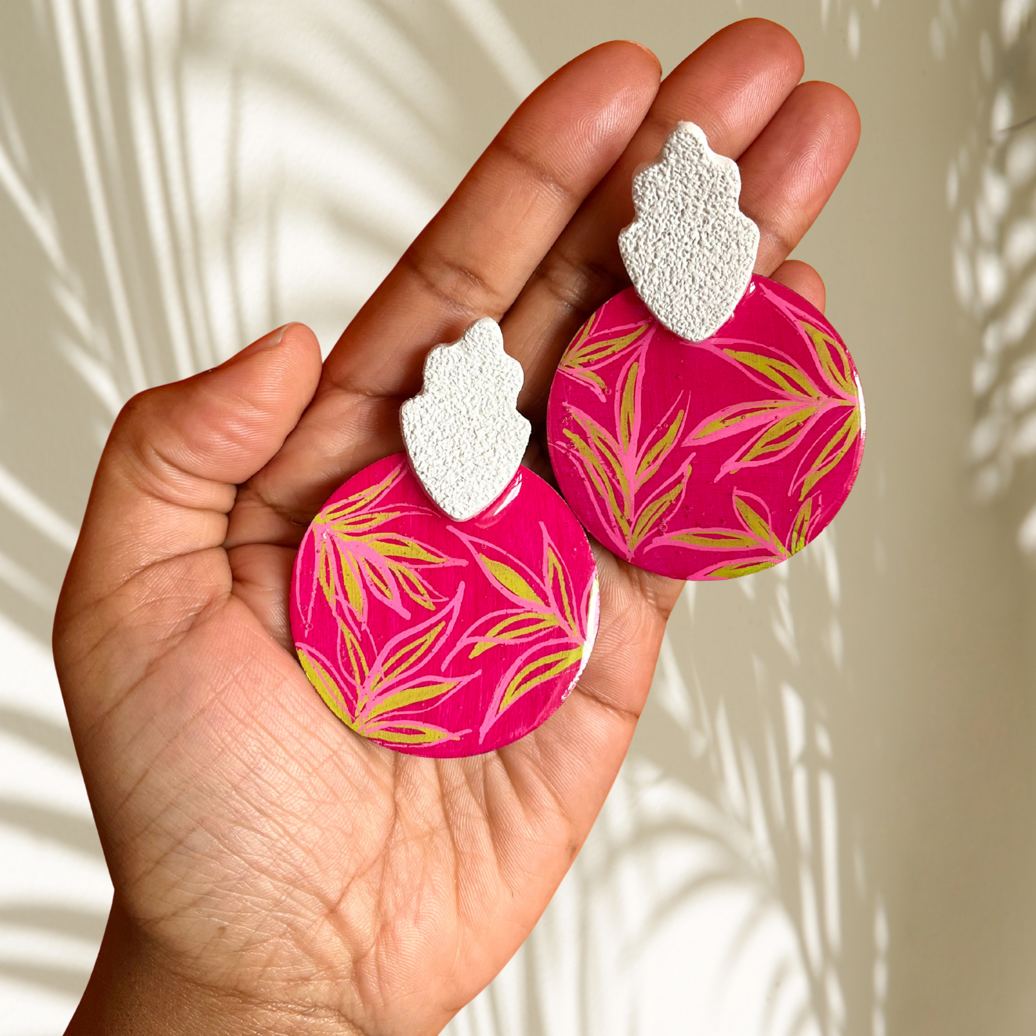 Hand holding pink earrings with leaf pattern against a neutral background
