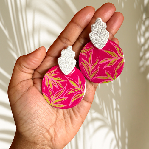 Hand holding pink earrings with leaf pattern against a neutral background