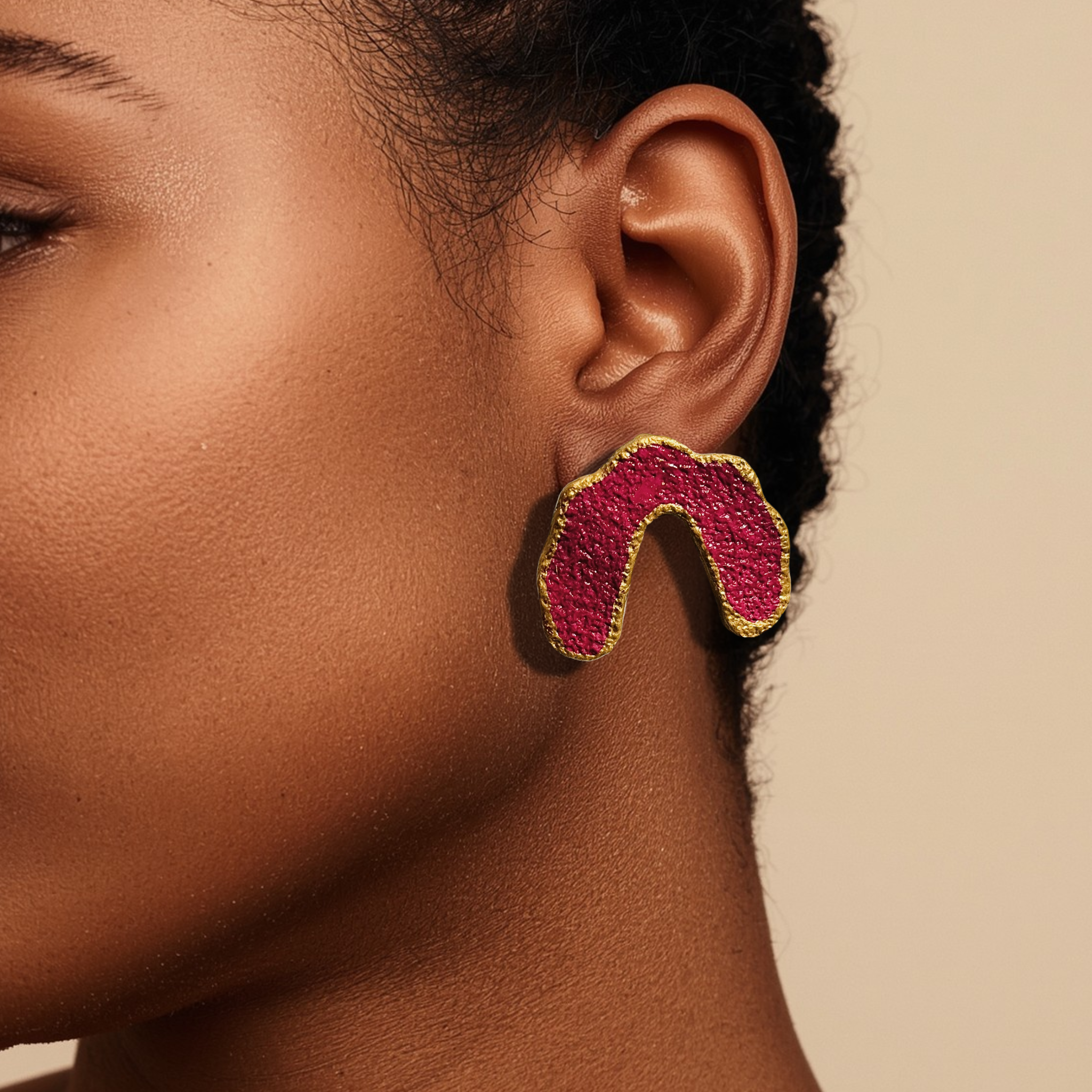 Close-up of an ear wearing a pink and gold earring against a beige background