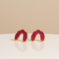 A pair of gold-framed, textured magenta-pink U-shaped stud earrings resting on a white reflective surface against a warm beige background.