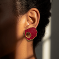 Close-up of an ear wearing a red earring with gold accents.