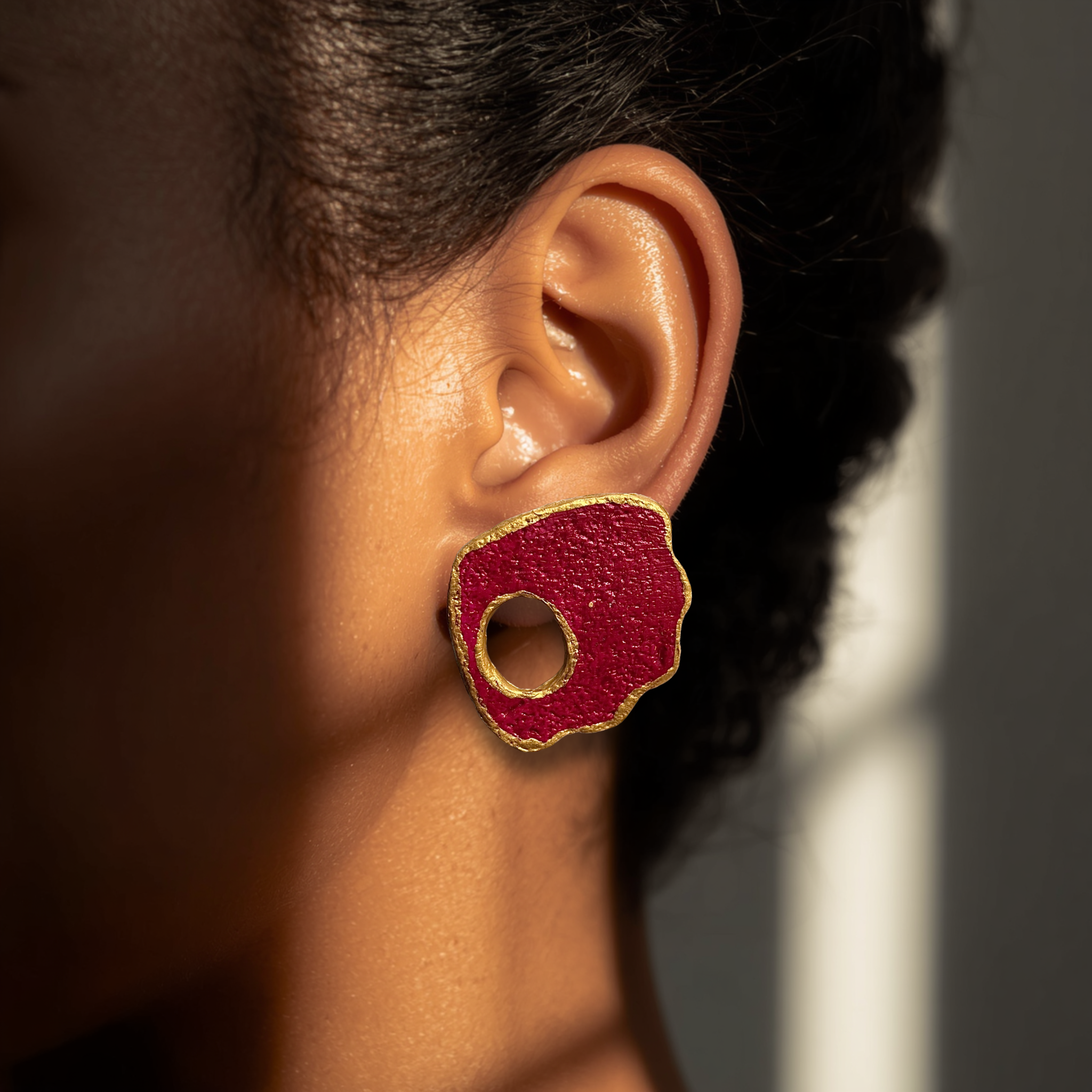 Close-up of an ear wearing a red earring with gold accents.
