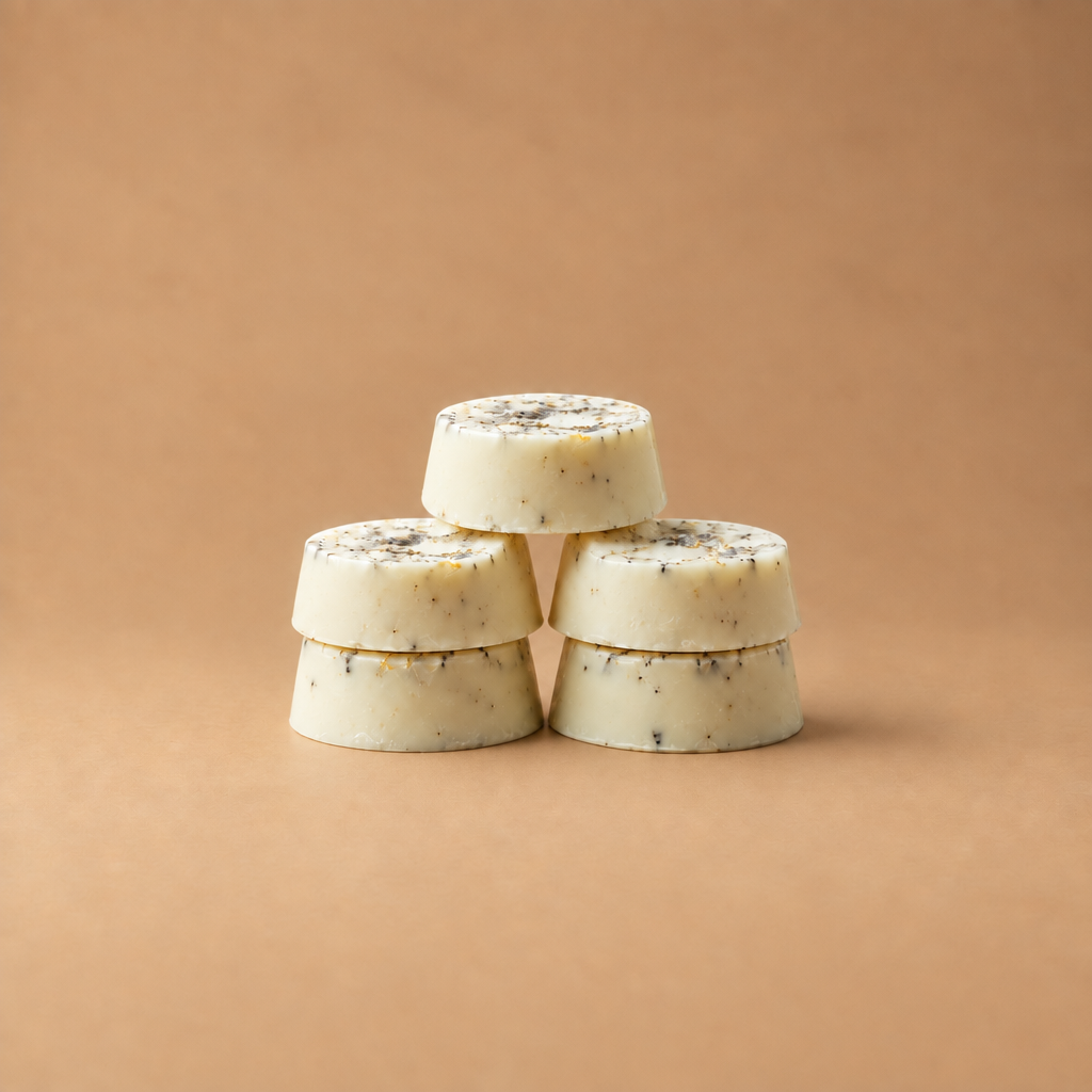 Six round off-white soap bars with black and yellow speckles, arranged on a light wood surface.